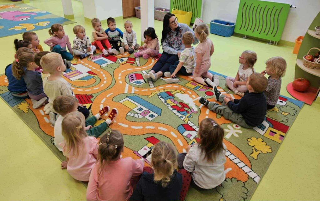 dzieci siedza na dywanie z kobietą która trzyma książkę