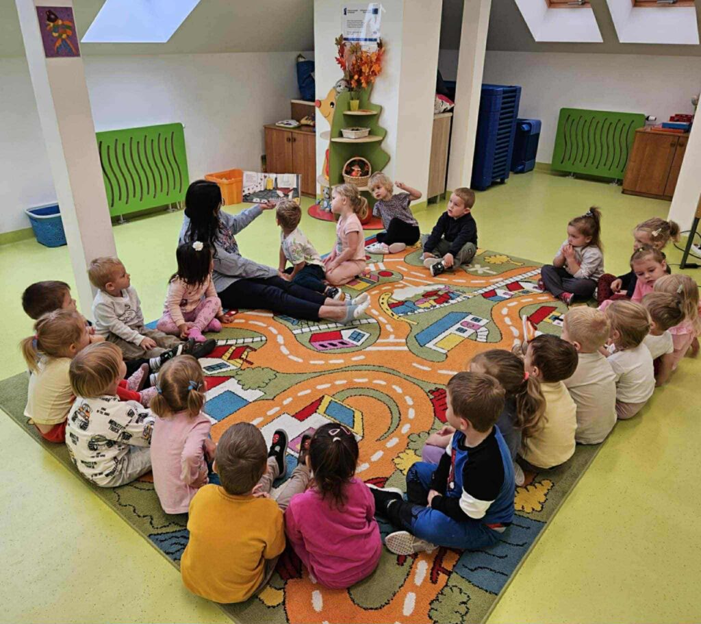 dzieci siedza na dywanie z kobietą która trzyma książkę