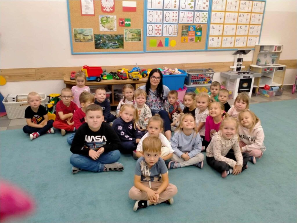 dzieci siedza na dywanie z kobietą która trzyma książkę