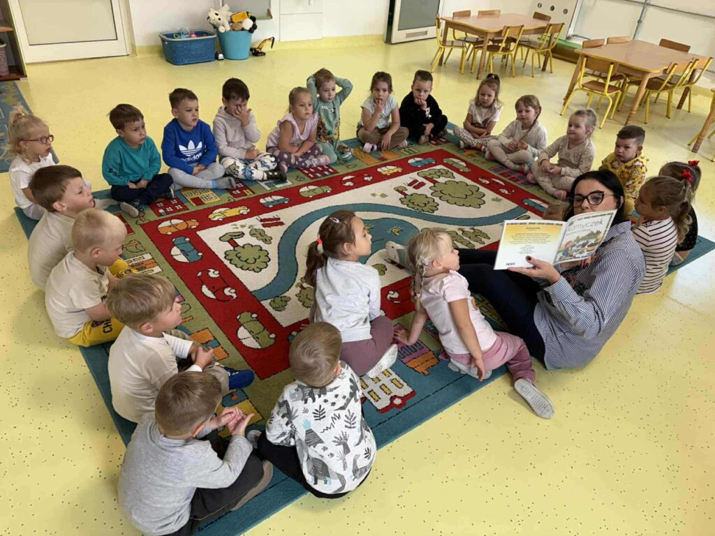 dzieci siedza na dywanie z kobietą która trzyma książkę